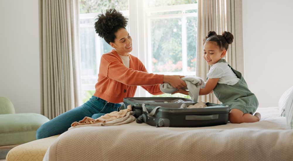 woman sitting on bed with little girl and suitcase